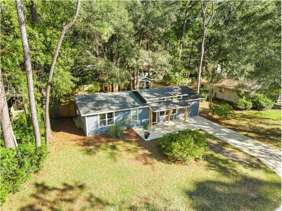 Aerial view of a blue-gray single-story home on a wooded lot in Gainesville